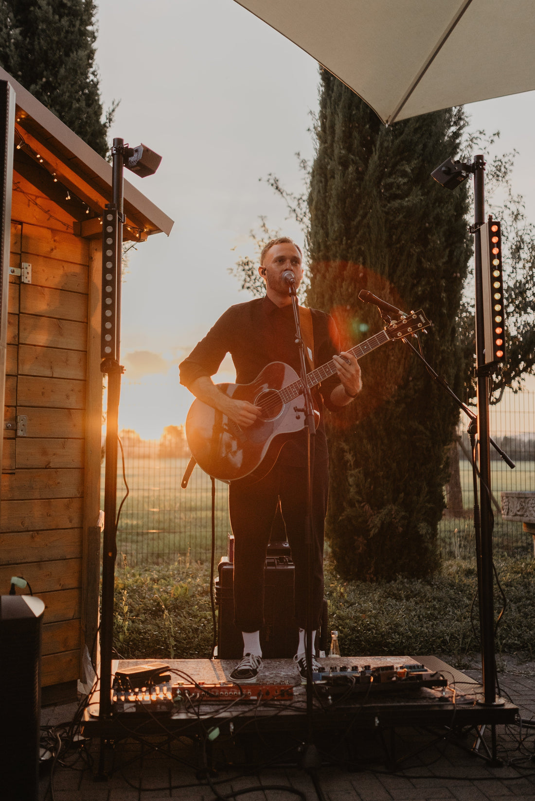 Musiker Marco - Live mit Gitarre, auf kleiner Bühne mit Licht und Sonne im Hintergrund.